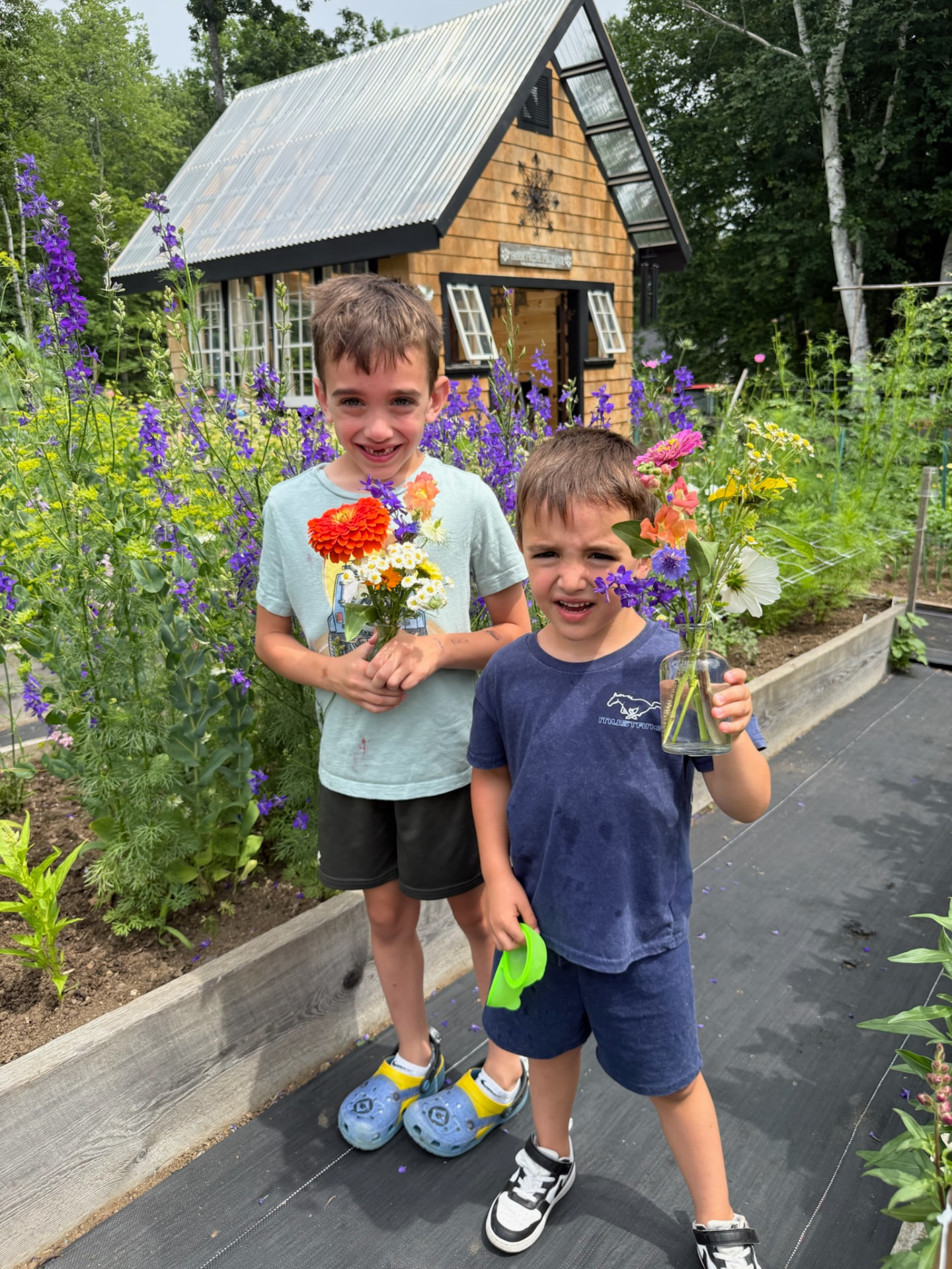 Two children carrying their own cut-flower bouquets through the garden rows
