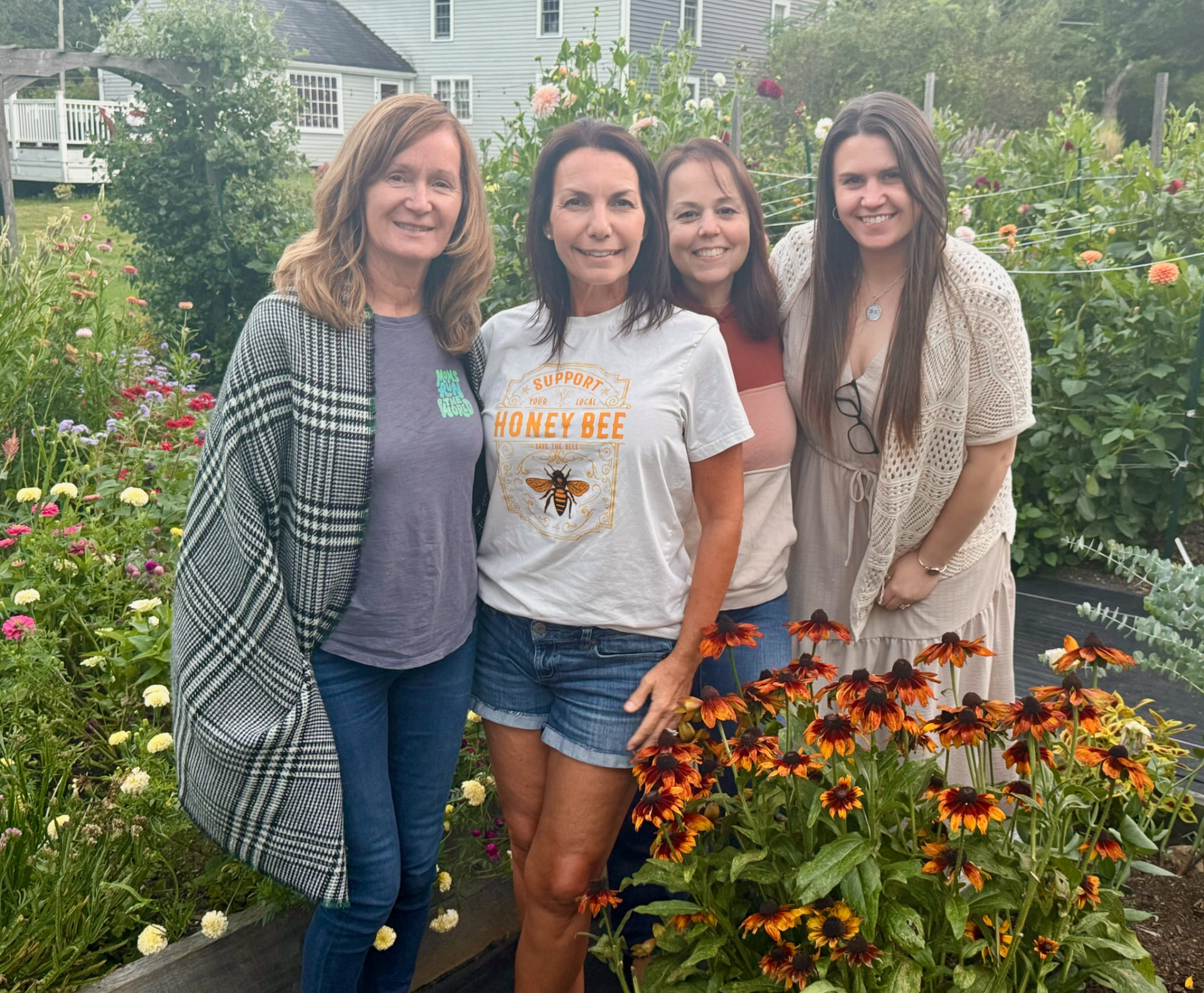 Four friends standing together smiling in the flower garden beside the coneflowers